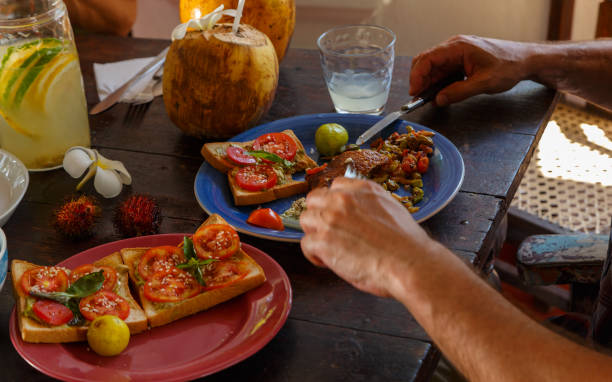 istock men's hands with a knife and fork on an authentic wooden table, man having Breakfast, in the background coconut, lemonade, fruit. The concept of healthy eating. 1213774345