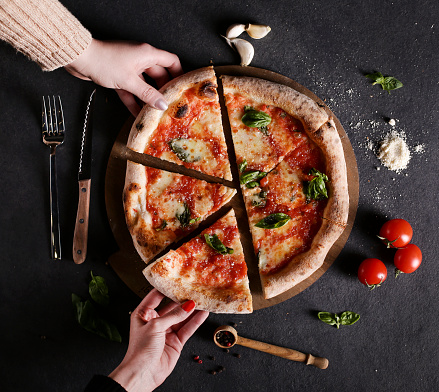 Friends sharing a delicious pizza, they are holding a slice, top view