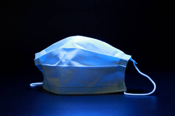 Blue Light On Medical Face Mask On A Dark Background. Protects Against Virus. Concept Of Air Pollution, Pneumonia Outbreaks, Coronavirus Epidemics, And The Risk Of Biological Contamination.
