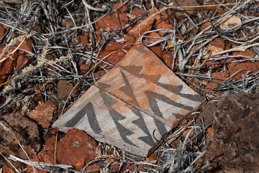 Nearly a thousand years ago natives inhabited the lower elevations around the San Francisco Peaks of Arizona.  In an area so dry it would seem impossible to live, they built pueblos, harvested rainwater, grew crops and raised families.  Today the remnants of their villages dot the landscape along with other artifacts.  Decorated pottery such as the shard shown in the picture was likely not produced in the area where the shard was found.  This type of pottery was brought in for trading purposes by people from nearby tribes.  It is unlawful to remove shards from an archeological site.  They may be examined but must be returned to their original location.  These pottery shards were photographed on South Mesa in Wupatki National Monument near Flagstaff, Arizona, USA.