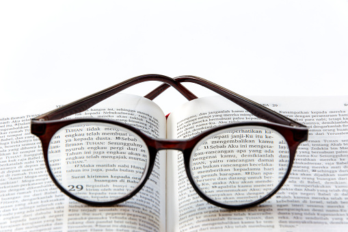 Open holy bible in bahasa Indonesia on white background with glasses