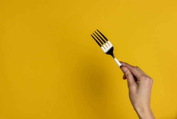 Female hand holds a fork on a yellow background. Top view. Studio shot stock photo