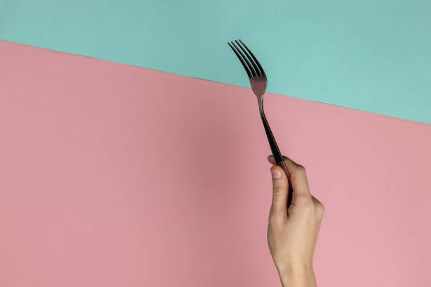 istock Female hand holds a fork on pink blue pastel background. Top view. Studio shot 1213800559