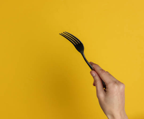 istock Female hand holds a fork on a yellow background. Top view. Studio shot 1213800570