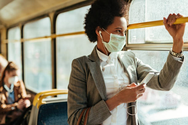African American businesswoman with face mask texting on the phone while traveling by bus. Black businesswoman with protective face mask using smart phone and looking through the window while commuting by bus. avian flu virus photos stock pictures, royalty-free photos & images
