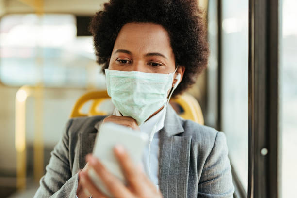 istock Black businesswoman with face mask using smart phone while communicating to work by bus. 1213801664