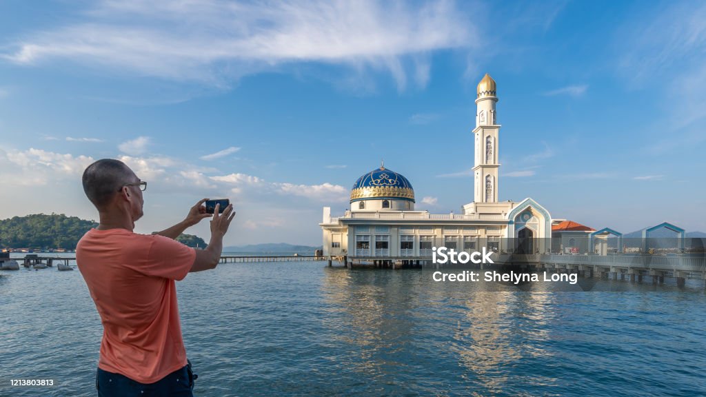 An Asian man photographing the floating mosque located in Pangkor Island through mobile phone An Asian man photographing the floating mosque located in Pangkor Island through mobile phone. the photo was taken in Malaysia. 40-49 Years Stock Photo