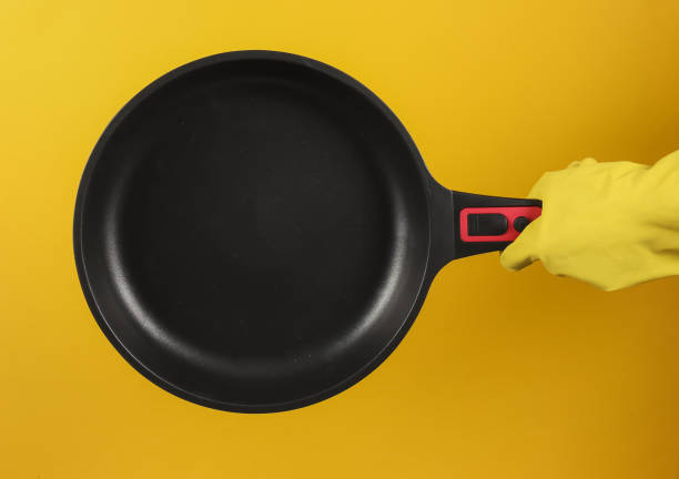 istock Hand in a rubber glove holds non-stick pan on yellow background. 1213804856
