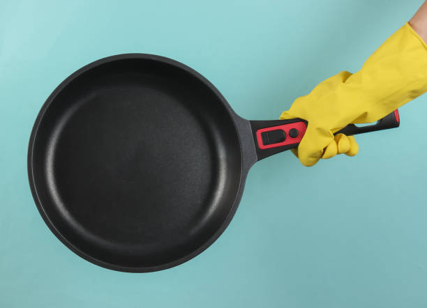 istock Hand in a rubber glove holds non-stick pan on a blue background. 1213804868