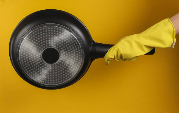 istock Hand in a rubber glove holds non-stick pan on yellow background. 1213804878