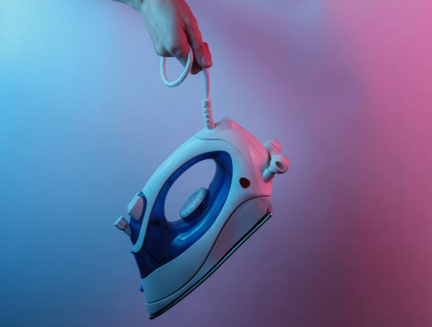 Hand holds iron for ironing by cable. Creative pop art pink blue neon color. Trendy gradient illumination. Night light