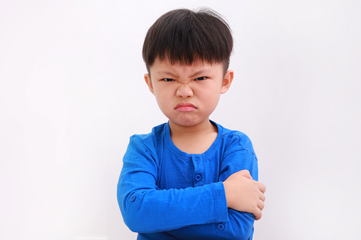 Portrait of little Asian boy with blue t-shirt, arm crossed, showing angry face, looking at the camera over white background.