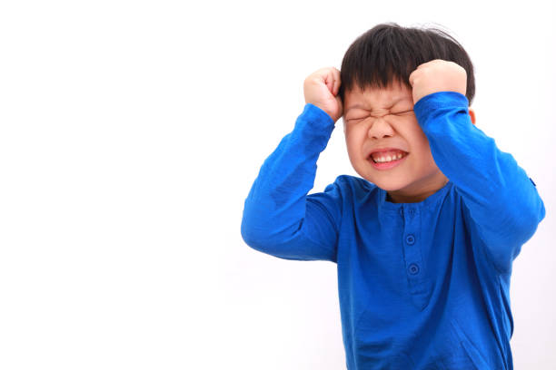 Frustrated little Asian boy against white background. stock photo