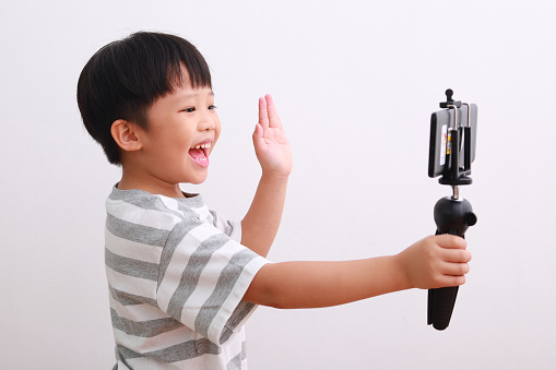 Portrait of little Asian boy blogger is filming video blog again white background.