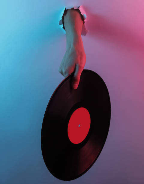 istock Hand holding vinyl plate through torn hole. Creative pop art pink blue neon color. Trendy gradient illumination. Night light 1213806476