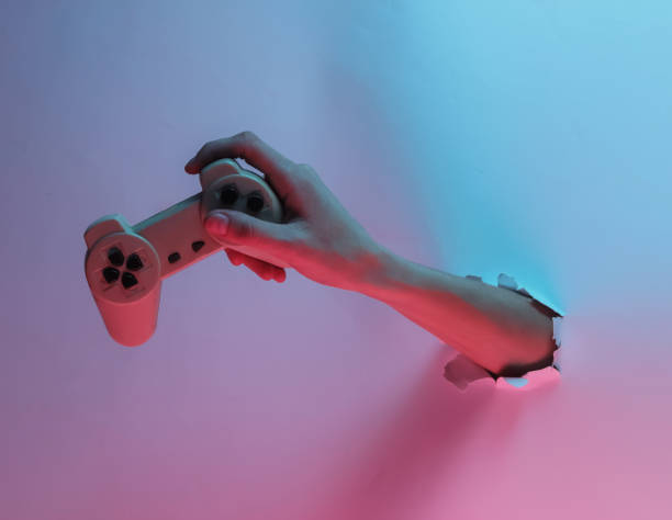 istock Hand holds gamepad through torn hole. Creative pop art pink blue neon color. Trendy gradient illumination. Night light 1213806478