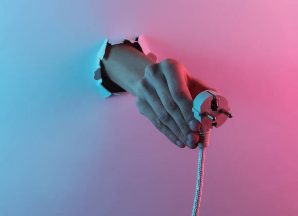 istock Hand holding electric plug through torn hole. Creative pop art pink blue neon color. Trendy gradient illumination. Night light 1213806507
