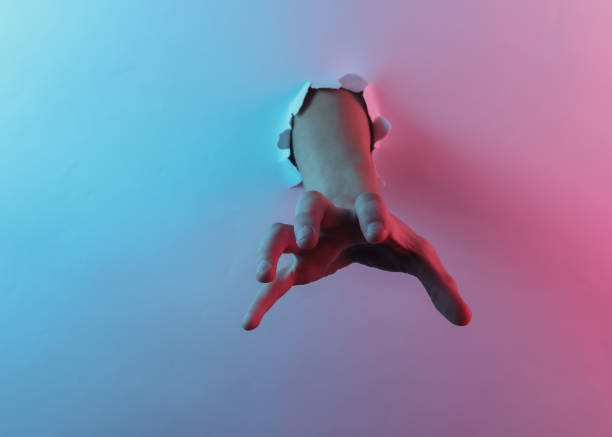 istock Mystical halloween concept. Hand through a torn hole. Creative pop art pink blue neon color. Trendy gradient illumination. Night light 1213806544
