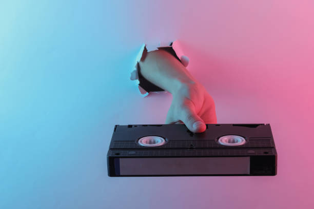istock Hand holding video cassette through torn hole. Creative pop art pink blue neon color. Trendy gradient illumination. Night light 1213806556