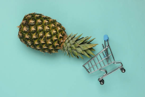 istock Shopping trolley and pineapple on a blue pastel background. Top view 1213806892