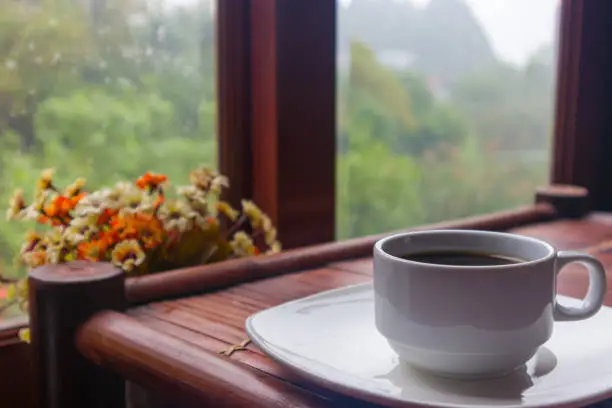 A cup of coffee on an old bamboo table with nature mountain view and flowervase