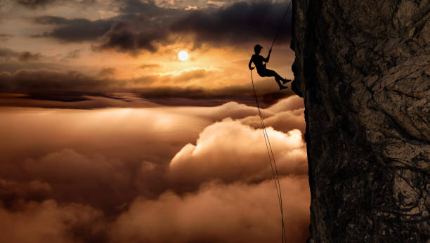 silhouette of a unrecognizable man rappelling down a steep cliff - climbing men sea cliff imagens e fotografias de stock