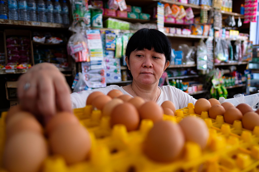 Asian Indonesian women arranging eggs inside small local family-owned business store, or locally called warung. Location is in Tasikmalaya, Indonesia. Selective Focus.