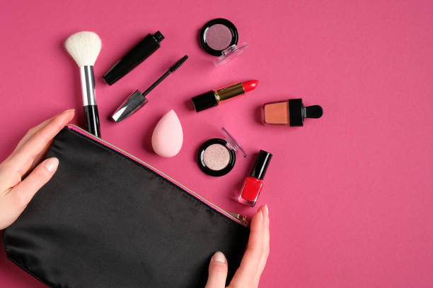 istock Cosmetic pouch with professional decorative cosmetics and makeup tools in female hands over pink background. Top view, flat lay. Beauty and fashion concept. 1213819792