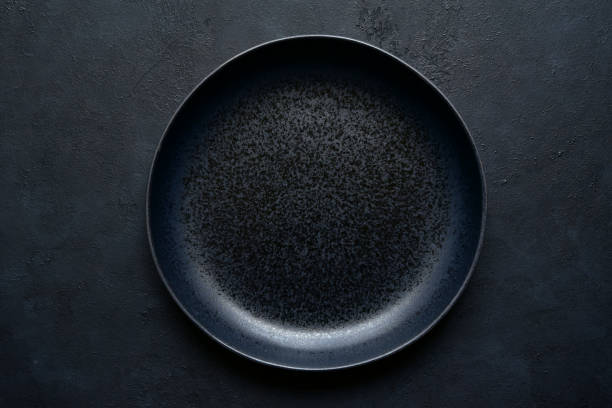 istock Culinary background with black empty plate on a dark slate, stone or concrete table. 1213824285