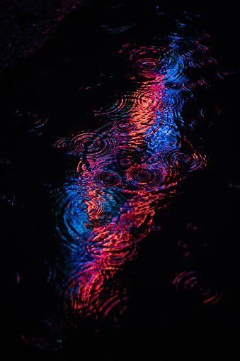 Reflection of a neon sign in a puddle on a rainy night in London