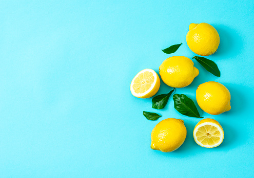 Ripe lemons flat lay with leaves on blue background. Copy space, top view