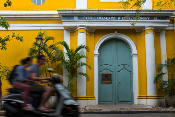 Unrecognisable couple on a scooter and yellow school building, Pondicherry stock photo