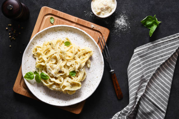 Tagliatelle pasta with cheese sauce and basil in a plate on the kitchen table. stock photo