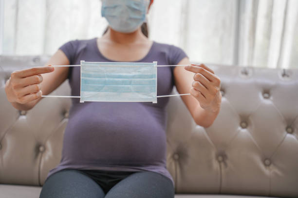 A pregnant woman wears a surgical mask to protect a COVID-19 (Coronavirus) and PM 2.5 and show a surgical mask on the abdomen to prevent infection to the fetus. stock photo