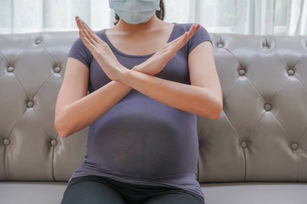 A pregnant woman wears a surgical mask to protect a COVID-19 (Coronavirus) and PM 2.5 and show stop sign shape by hand to prevent infection to the fetus. A pregnant woman wears a surgical mask to protect a COVID-19 (Coronavirus) and PM 2.5 and show stop sign shape by hand to prevent infection to the fetus. babyproof stock pictures, royalty-free photos & images
