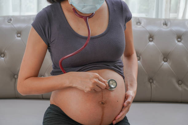A pregnant woman wears a surgical mask and checking her fetus by stethoscope. Protect a COVID-19 (Coronavirus), PM 2.5 and prevent infection to the fetus concept. stock photo