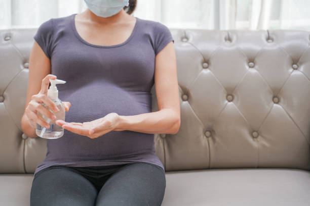 une femme enceinte porte un masque chirurgical se lave les mains par gel d’alcool sur le sofa. protégez un covid-19 (coronavirus), pm 2.5 et prévenir l’infection au concept de fœtus. - prenatal care photos et images de collection