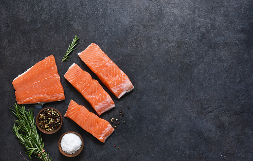 Fresh salmon filet and spices on a concrete black background. Ingredients for cooking.