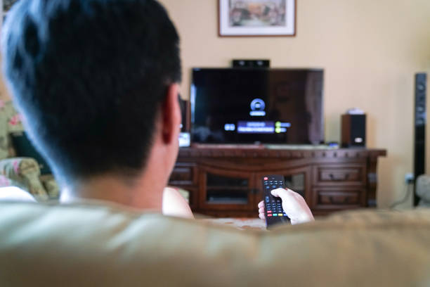 istock Man using remote control to watch TV at home 1213838322