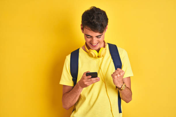 adolescente usando fones de ouvido e usando smartphone sobre fundo isolado gritando orgulhoso e celebrando vitória e sucesso muito animado, torcendo emoção - university education screaming shouting - fotografias e filmes do acervo