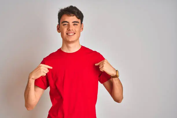 Photo of Teenager boy wearing red t-shirt over white isolated background looking confident with smile on face, pointing oneself with fingers proud and happy.