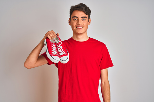 Teenager boy holding fashion and casual sneakers over red isolated background with a happy face standing and smiling with a confident smile showing teeth