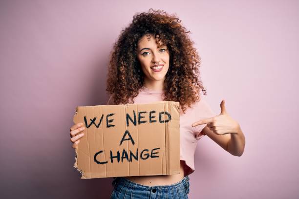 istock Young beautiful activist woman with curly hair and piercing protesting asking for a change very happy pointing with hand and finger 1213844395