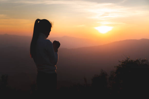 silhueta de jovens mãos humanas orando a deus ao nascer do sol, fundo conceitual da religião cristã. - praying girl - fotografias e filmes do acervo