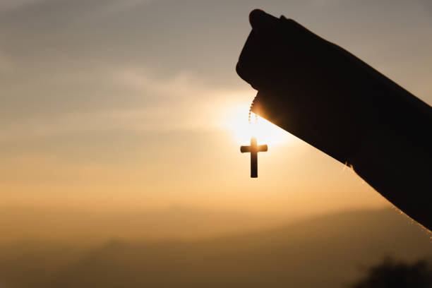 istock human hands praying to the GOD while holding a crucifix symbol with bright sunbeam. 1213848868