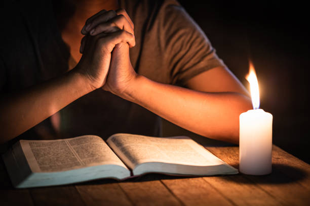 conceptos religiosos, el joven oró sobre la biblia en la habitación y encendió las velas para iluminar. - cross shape wood cross old fotografías e imágenes de stock