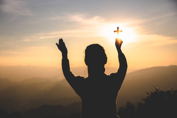 istock human hands praying to the GOD while holding a crucifix symbol with bright sunbeam. 1213849161