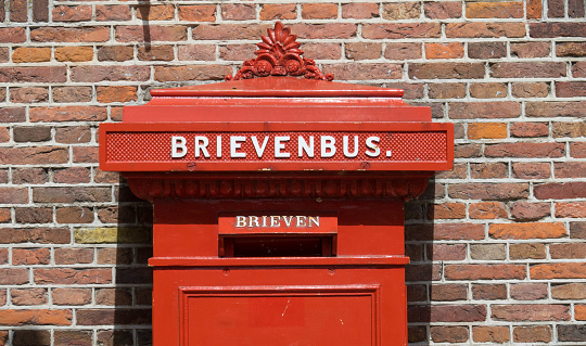 A red British post box against a hedge line or rural setting