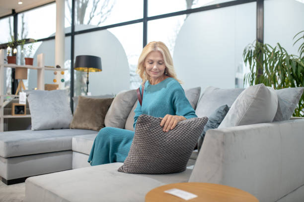 istock Blonde woman looking at a pillow while sitting on a sofa. 1213854213