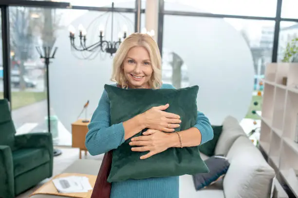 Photo of Beautiful woman hugging a green decorative pillow in a store.